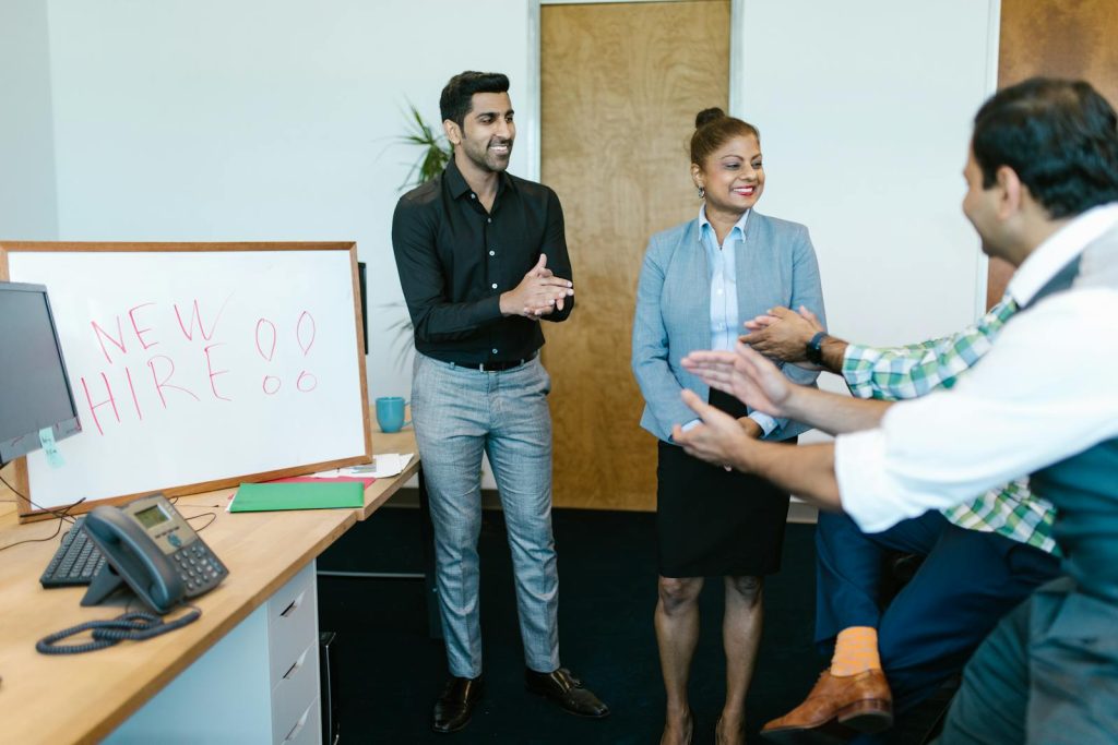 Colleagues joyfully applaud a new hire announcement in a modern office setting.